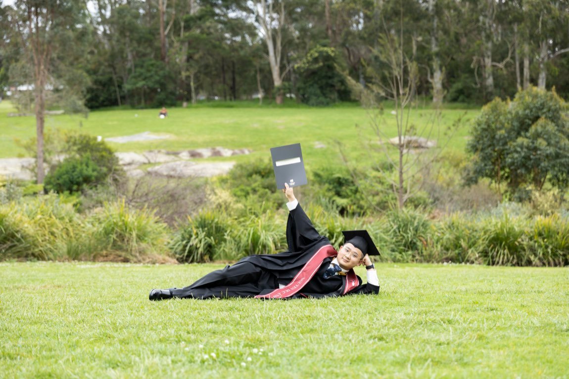 Graduate reclining on the lawn holding his diploma aloft