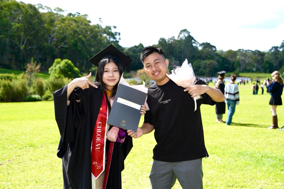 Graduate pointing at her folder while a friend holds it up